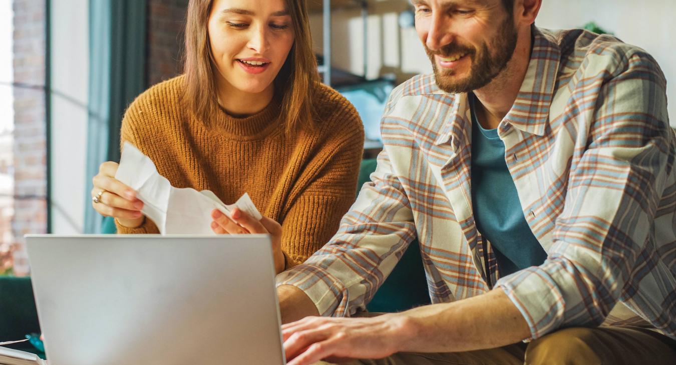 Young couple sitting at a table with a laptop and bills, deciding on their budget
